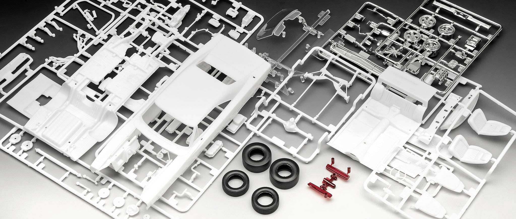 'Model car kit made from plastic parts, including bodywork, tyres and small components. Parts laid out on a metal background.'