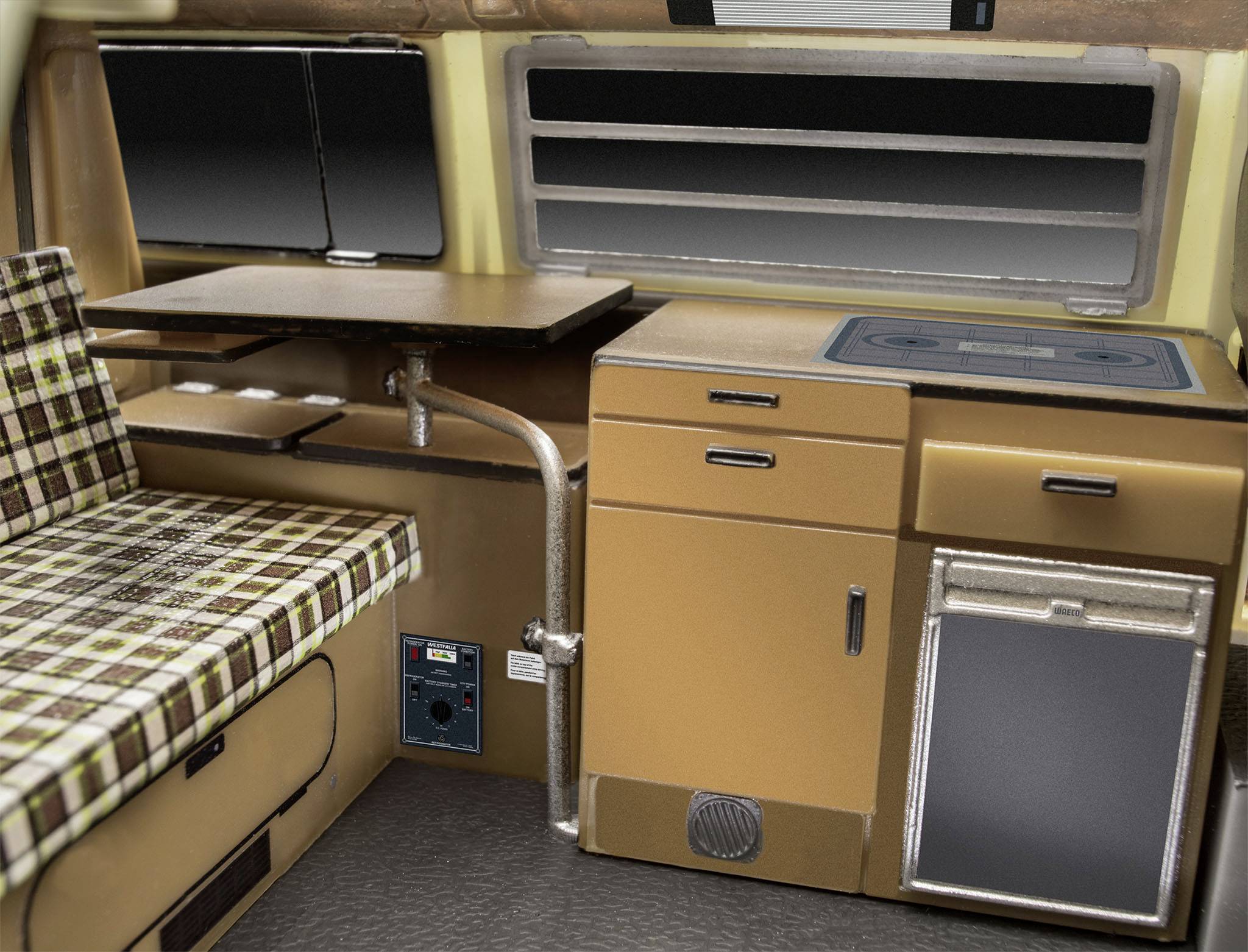 Interior of a motorhome with a seating bench and table on the left, kitchen area with cooker, cupboard and small fridge on the right.