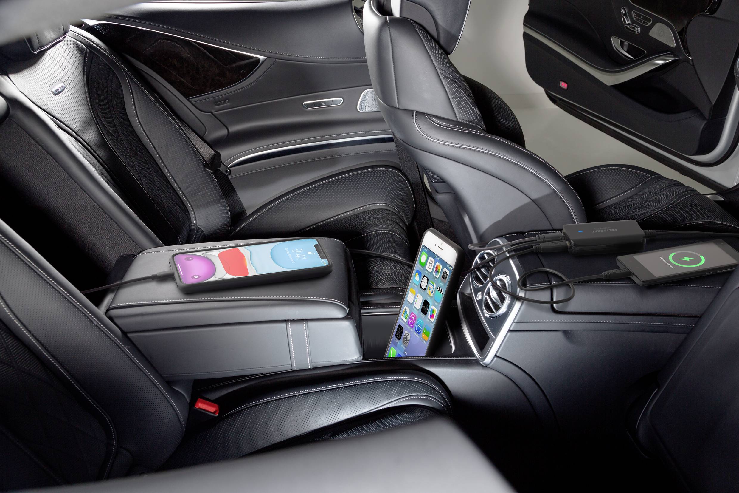 Luxurious car interior with black leather seats. Two smartphones are resting on the centre console, one charging via cable and the other charging wirelessly.