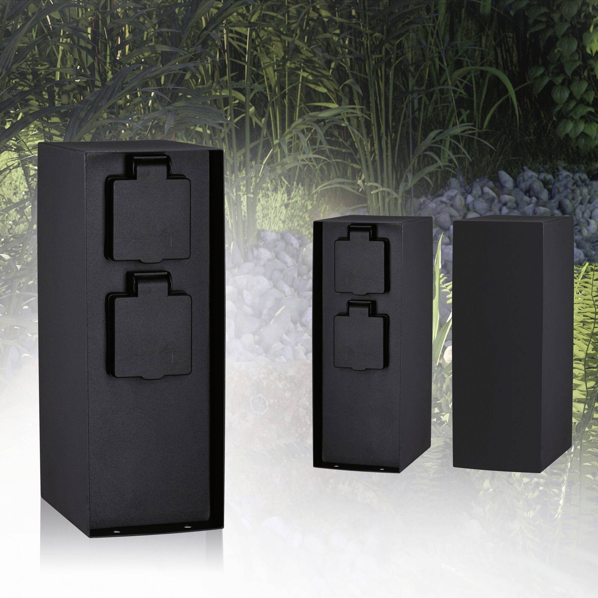 'Three black, rectangular socket columns outdoors, surrounded by plants and stones.'