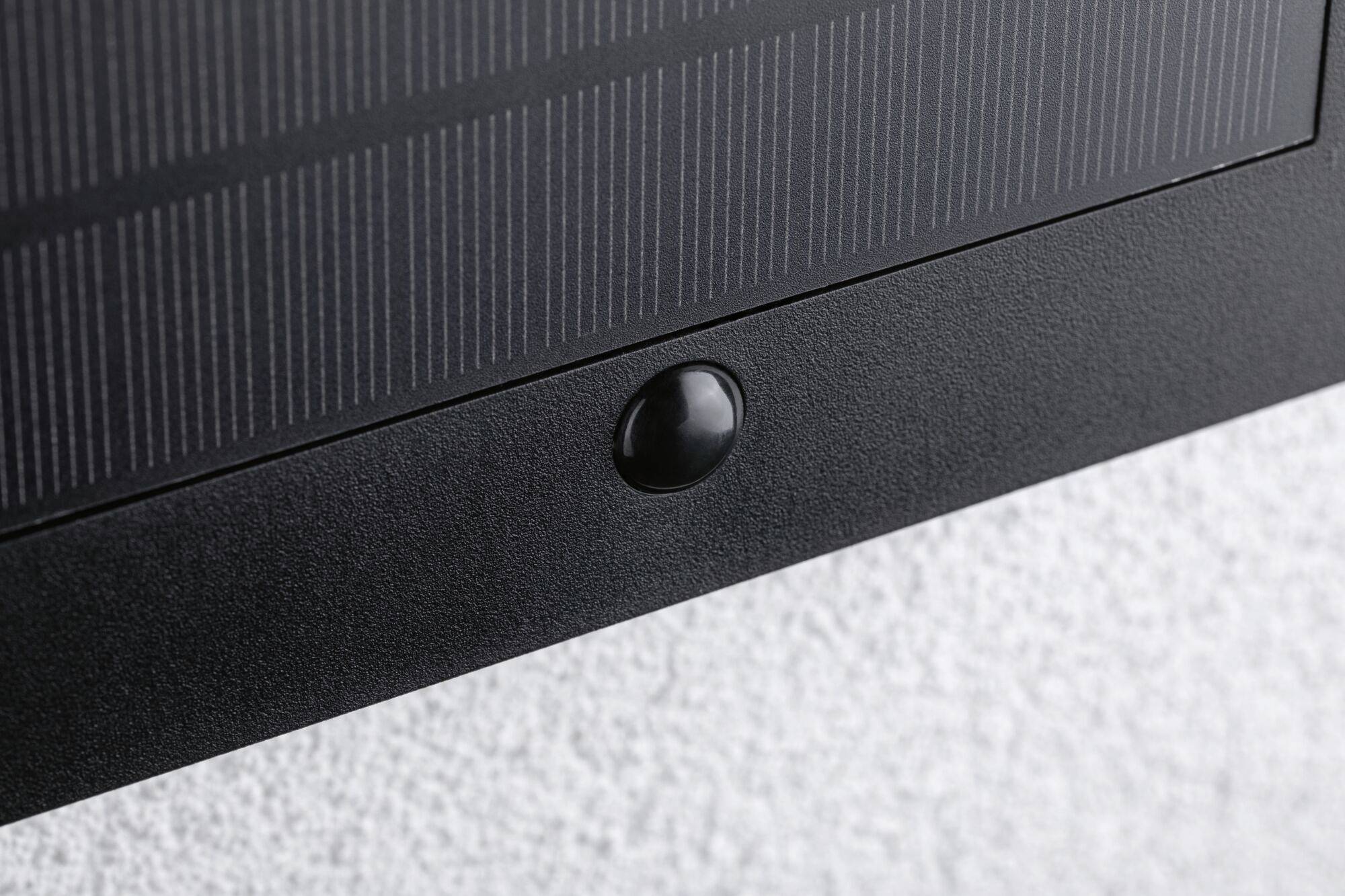 Close-up of a black button on an electronic device with a textured white surface in the background.