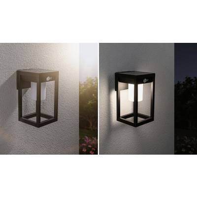 Wall light in a modern, square design, illuminating at dusk, mounted on an exterior wall with a garden in the background.