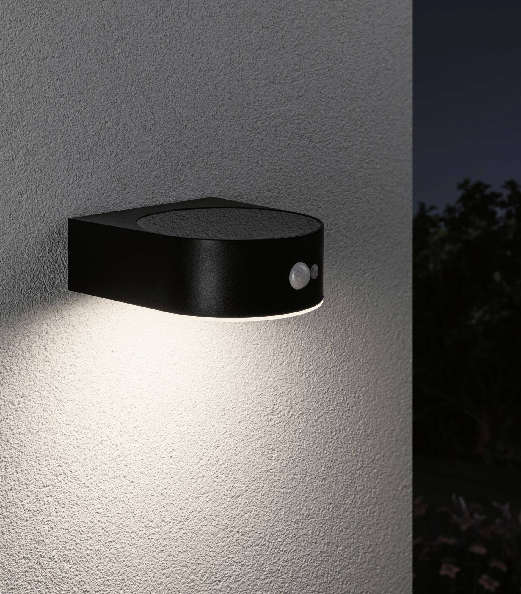 Exterior wall light with sensor illuminates a white wall while the surrounding area remains dark.