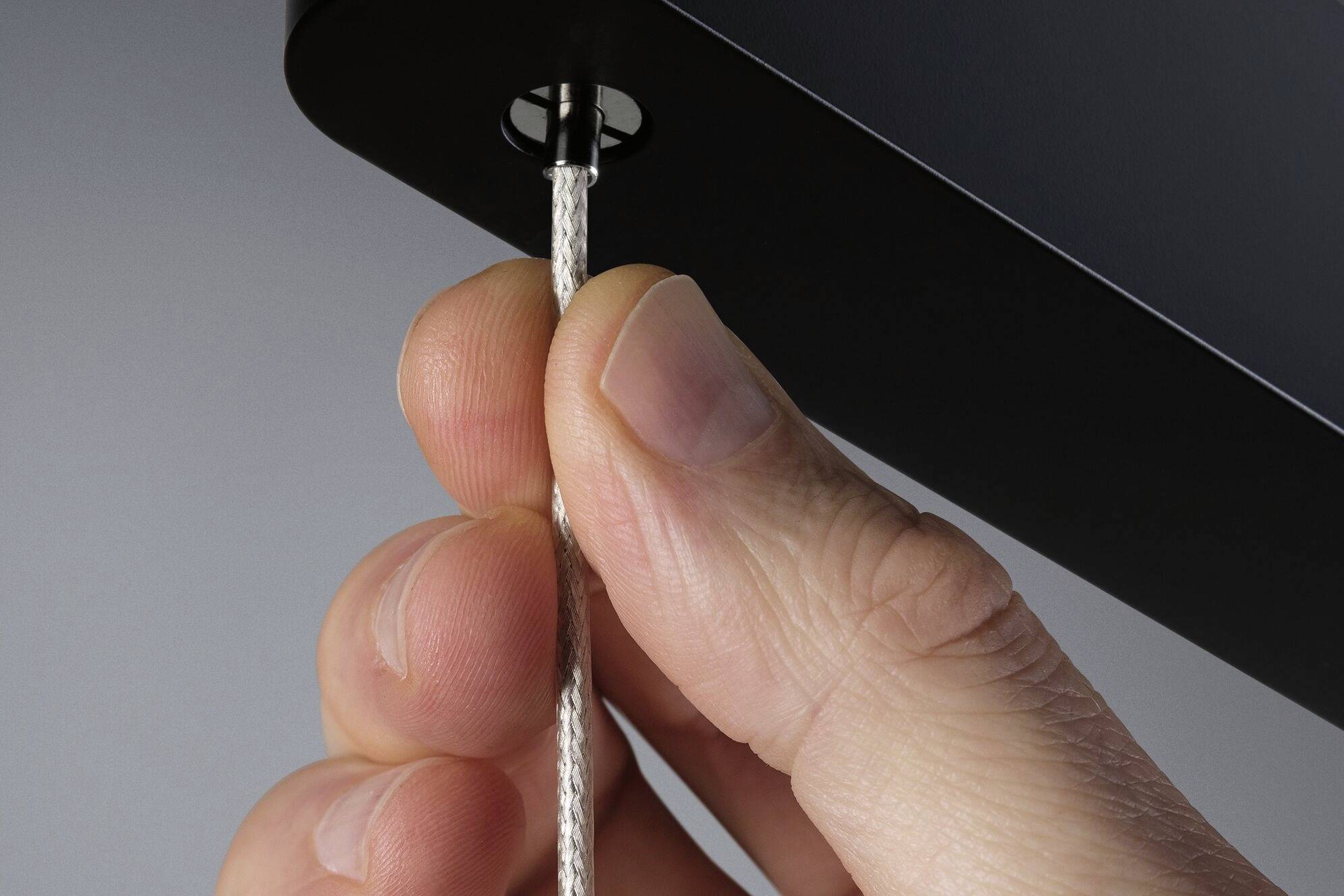 A finger pulls on a white cord emerging from a black casing.