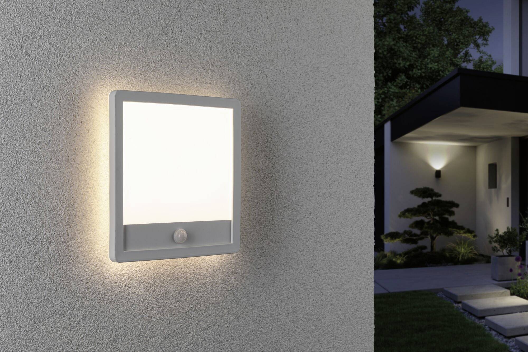 A rectangular wall light with a motion sensor illuminates a modern house façade at dusk.