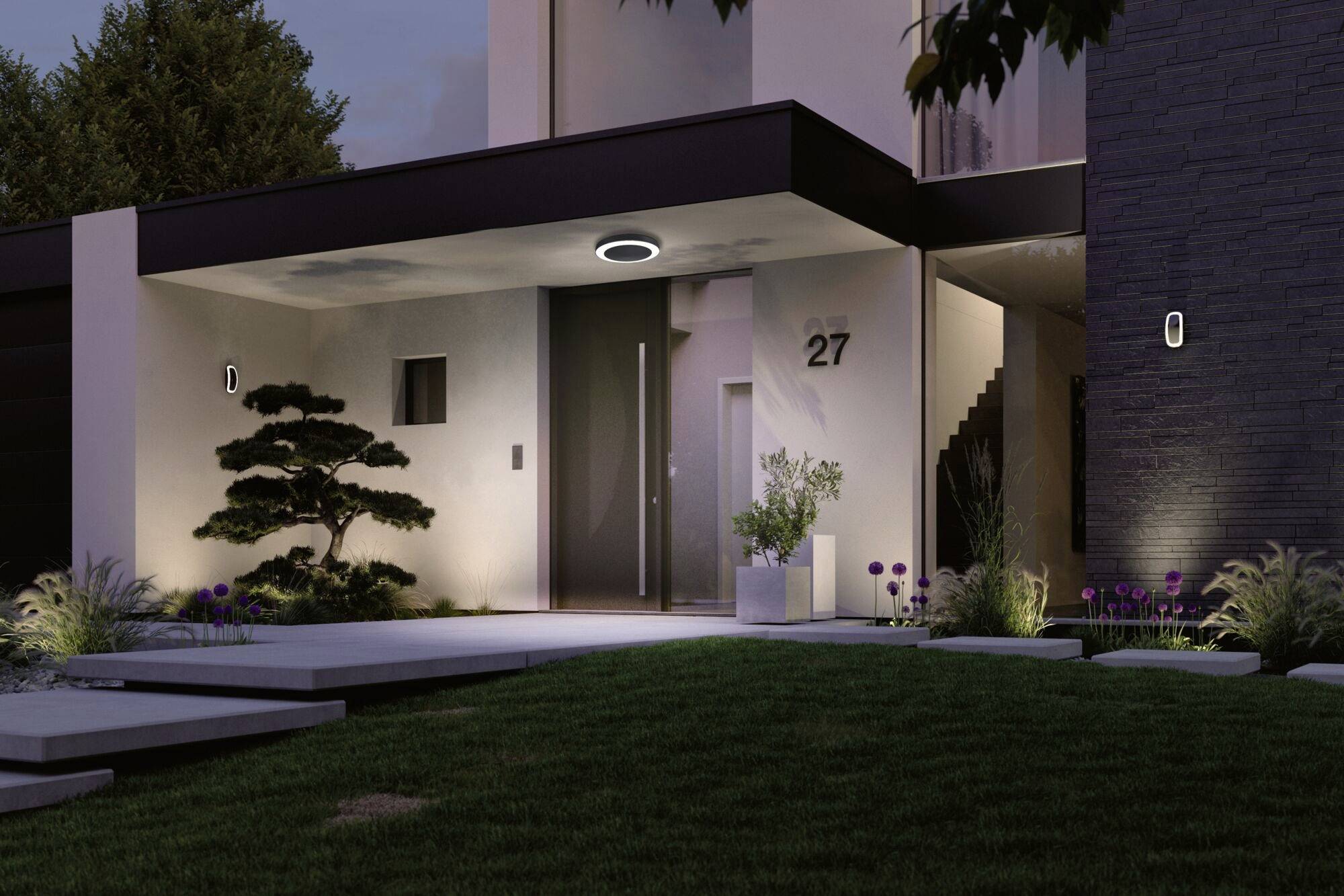 Modern house at dusk, illuminated entrance with stairs on the right, tree in the foreground, plants and house number 27 visible.