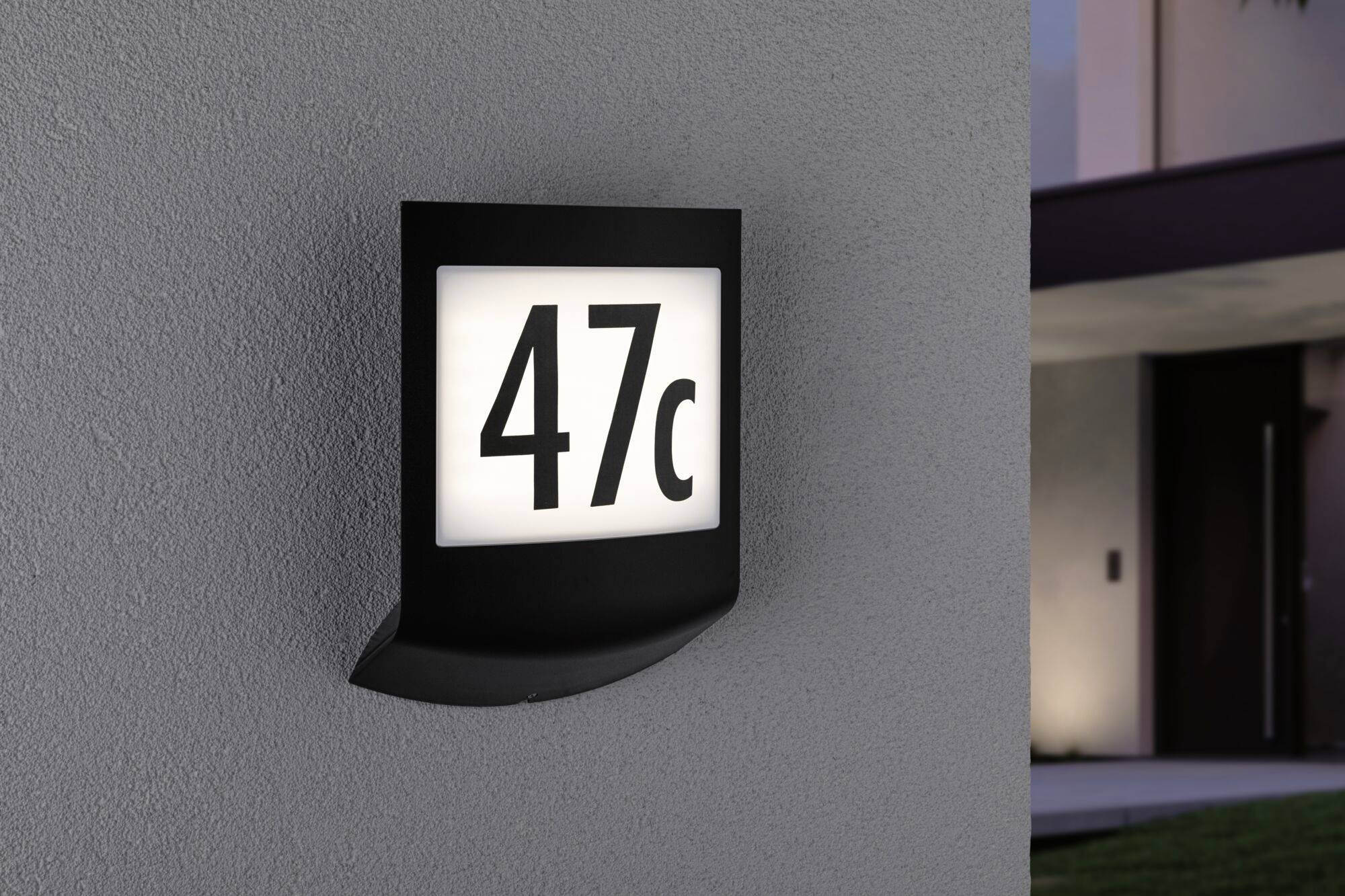 Illuminated house number sign on a grey wall displays '47c'. Background slightly blurred, suggesting a modern building.