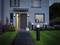 A modern house with an open door, revealing an illuminated path and a garden with flowers. A sign displays '47c'.