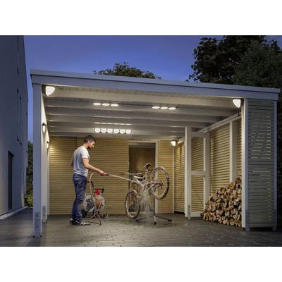 A man is cleaning a muddy bicycle with a pressure washer under a covered area next to a wood pile.