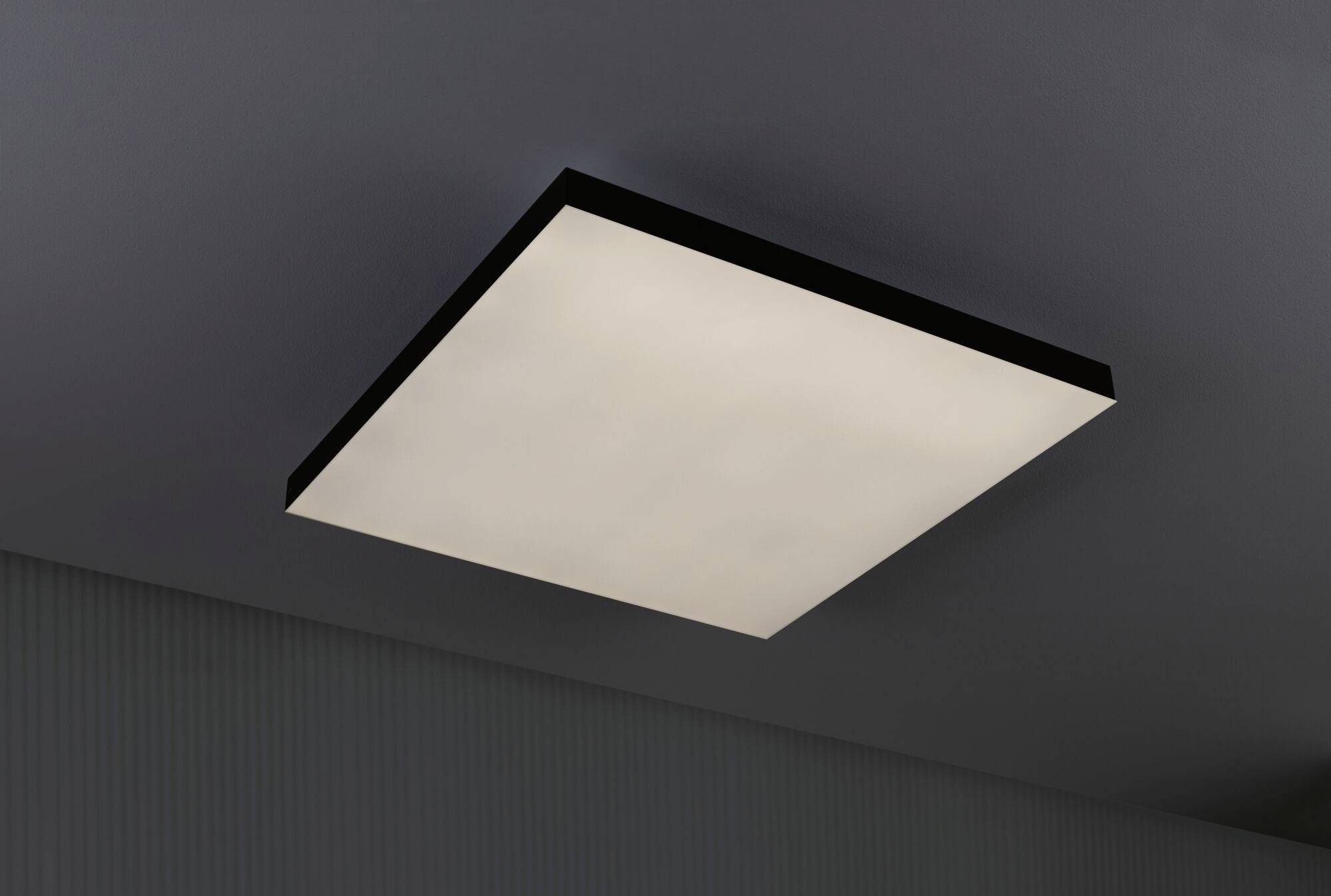 Square ceiling light with a black frame emits white light. It is mounted on a grey ceiling.
