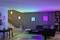 A modernly furnished living room with a sofa, a table and atmospheric, colourful wall lighting.
