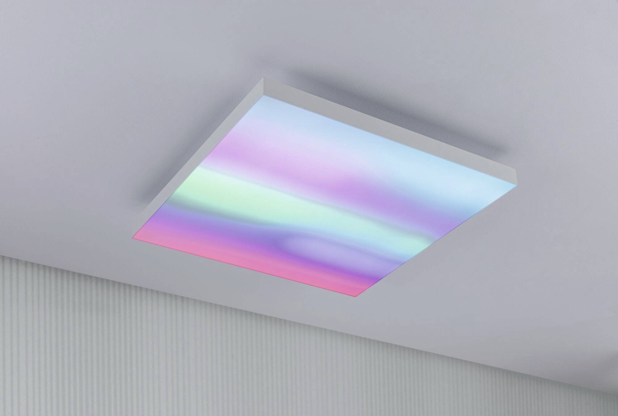 A ceiling lamp with softly changing colours in pastel shades illuminates a modern, minimalist room.