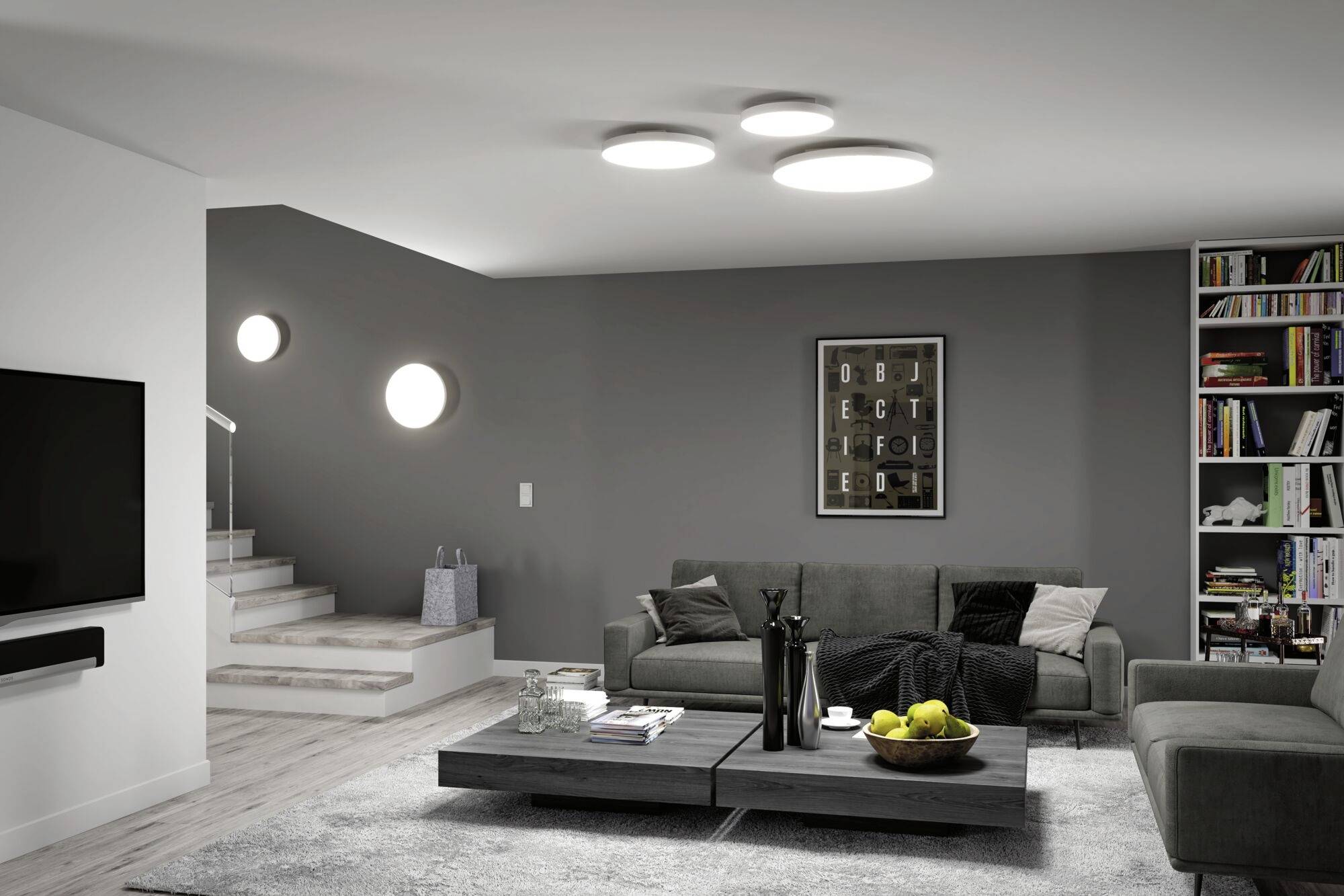Modern living room design with a grey sofa, coffee table, wall art and bookshelf. Bright ceiling lights and stair access.