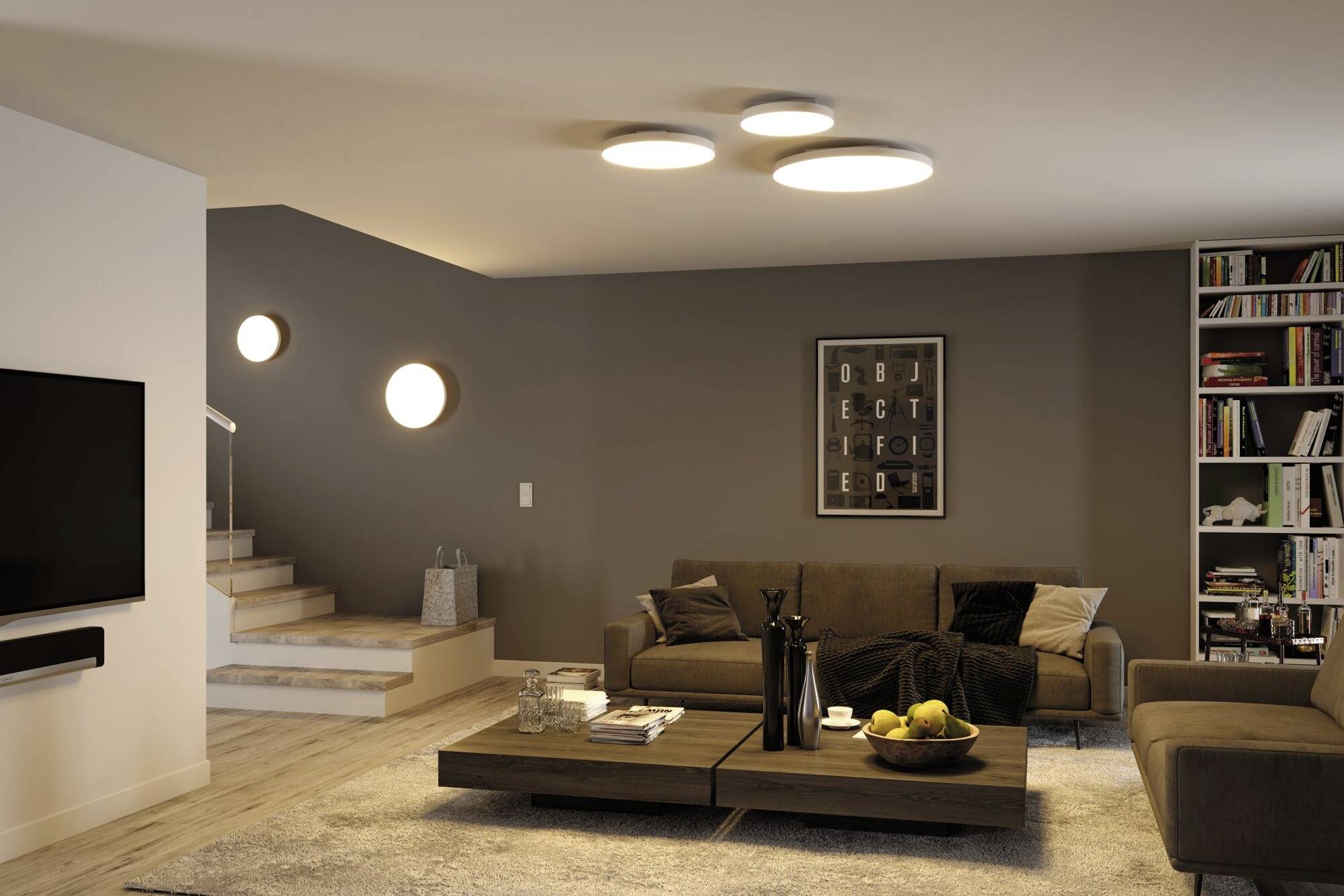 A modern living room with a grey sofa, coffee table and bookshelf. Circular light fixtures and a picture with letters are mounted on the wall.