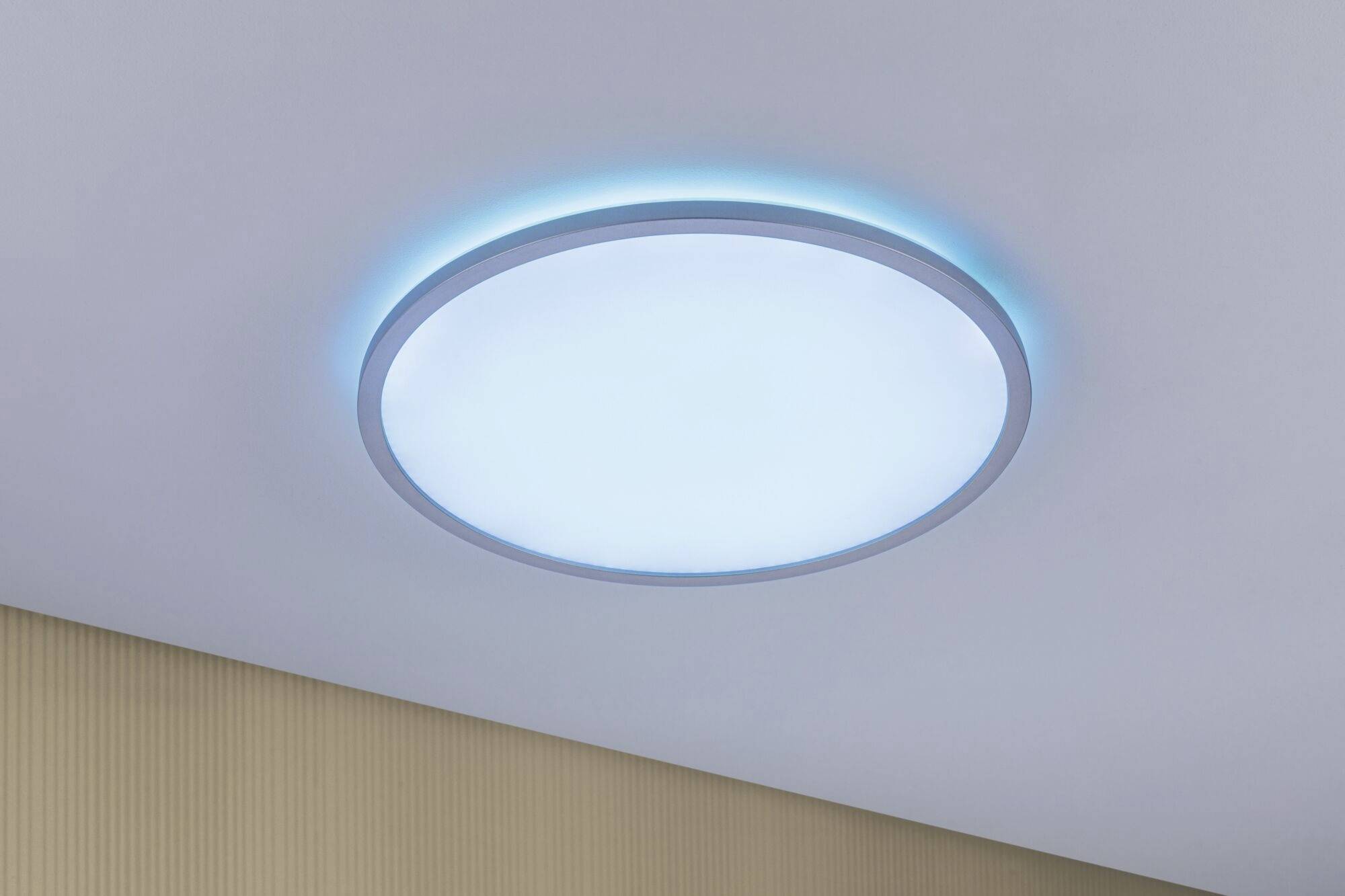 A circular ceiling light emits blue and white light and is mounted on a white ceiling.