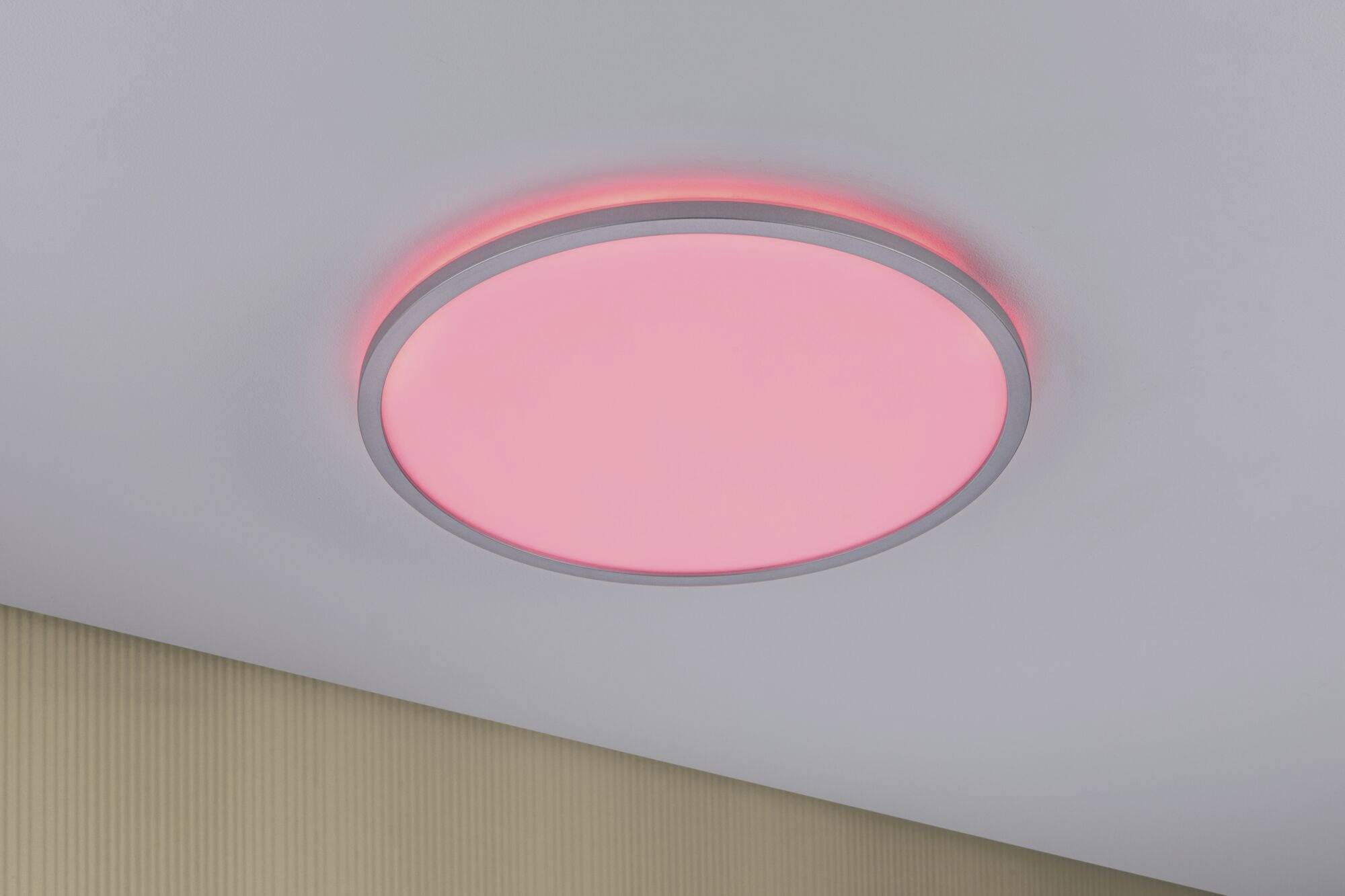 A round ceiling light emits a warm, red glow. It is installed against a white ceiling and a beige wall.