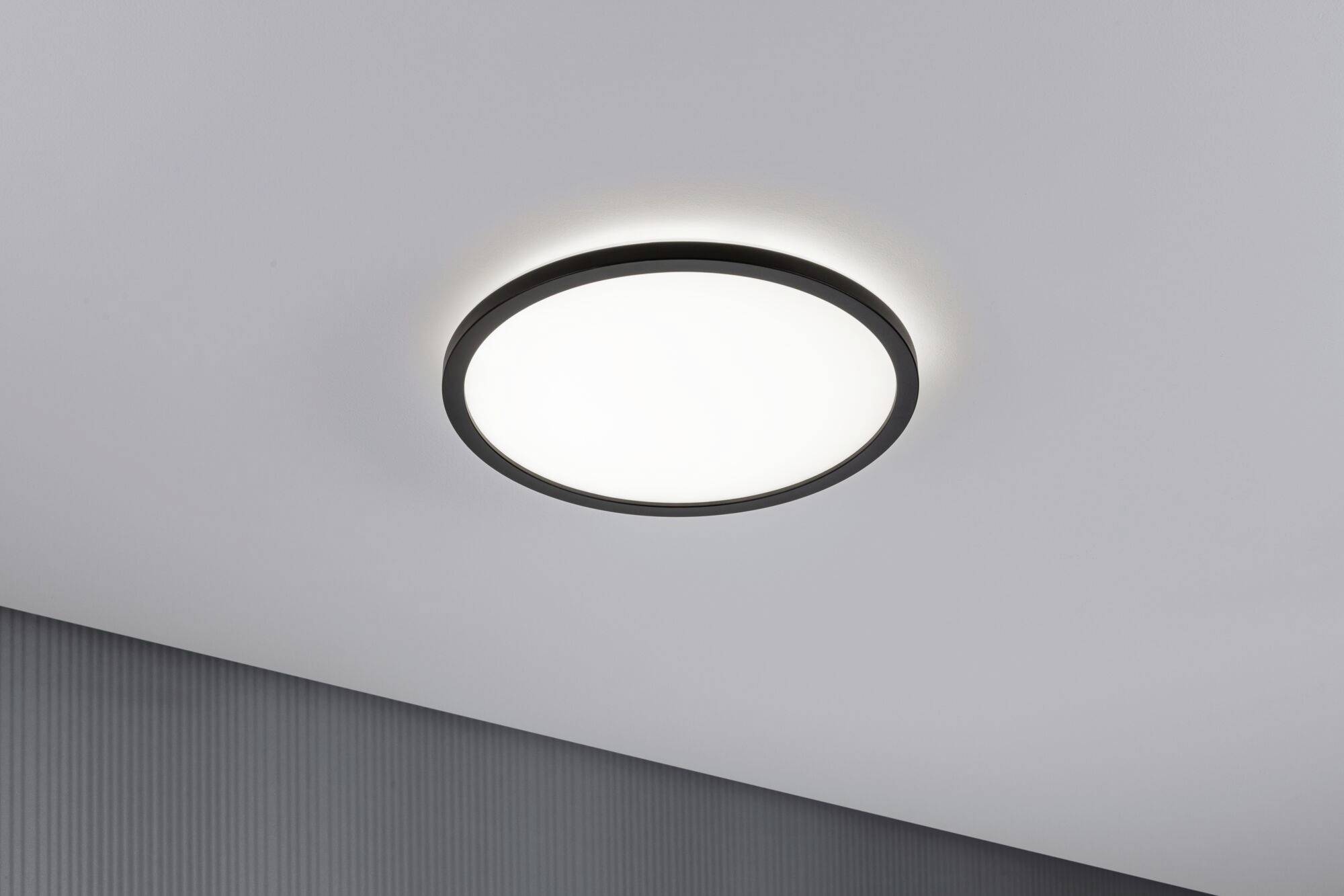 A round ceiling light with a black frame, emanating soft light in a modern room.