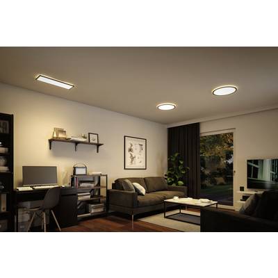 A modern living room with a dark sofa, a coffee table, a desk with a computer and shelves, illuminated by ceiling lights.