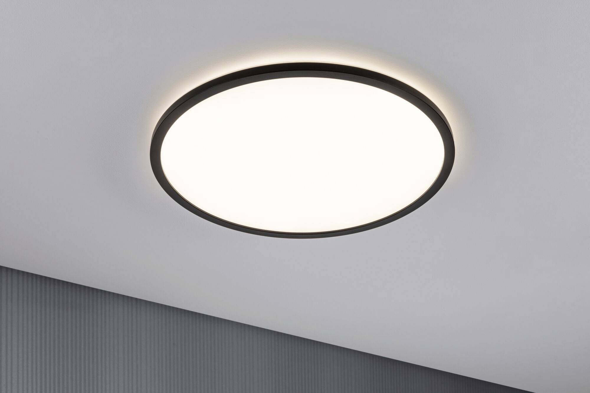 Round ceiling light with a black frame mounted on a grey ceiling, shining brightly and evenly.