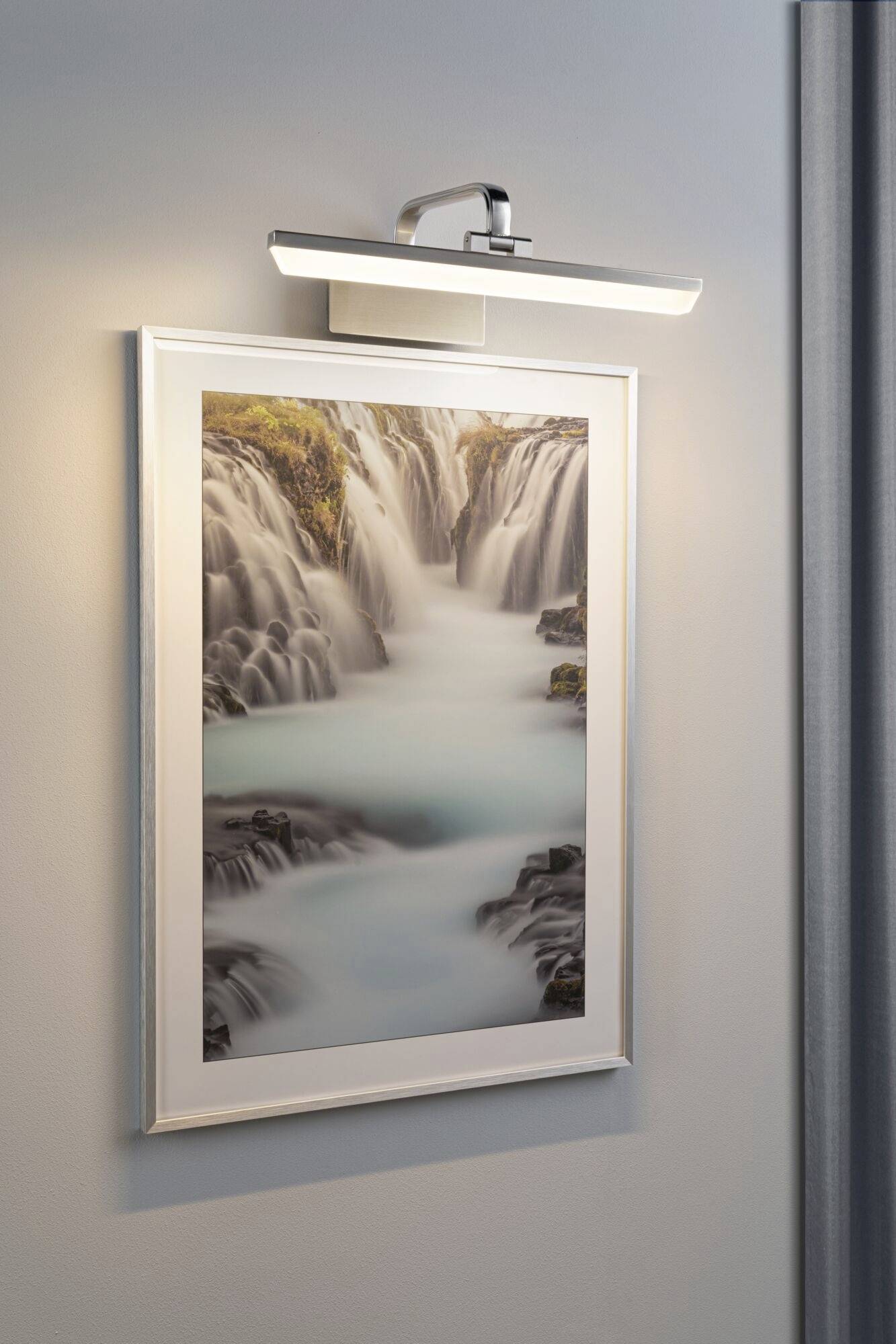 Framed picture of a waterfall, illuminated on a wall.