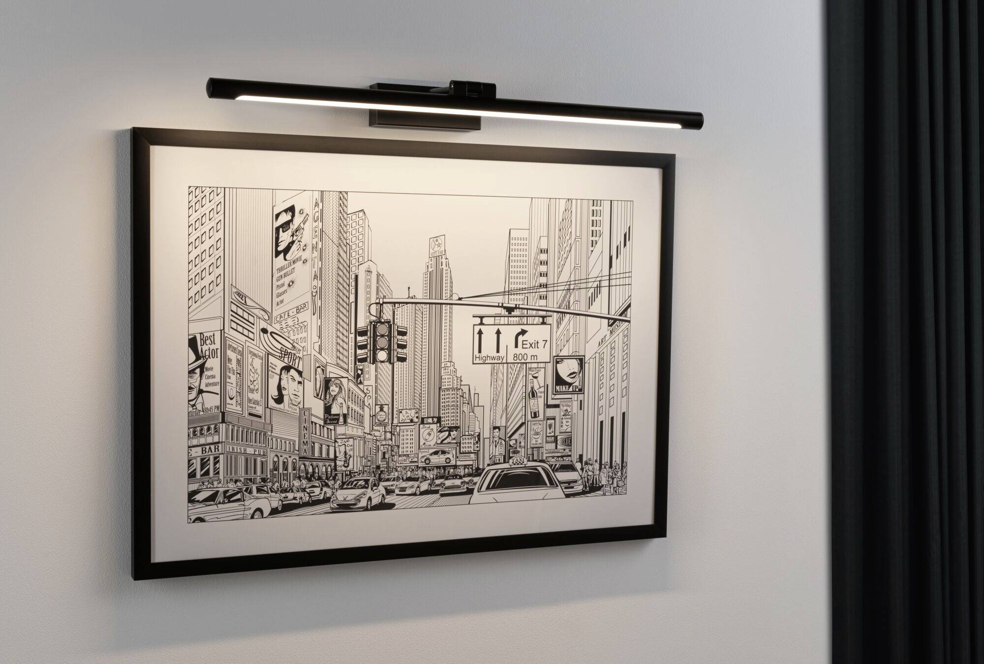 Black and white drawing of a bustling city street with cars and tall buildings. Illuminated and hanging on the wall.