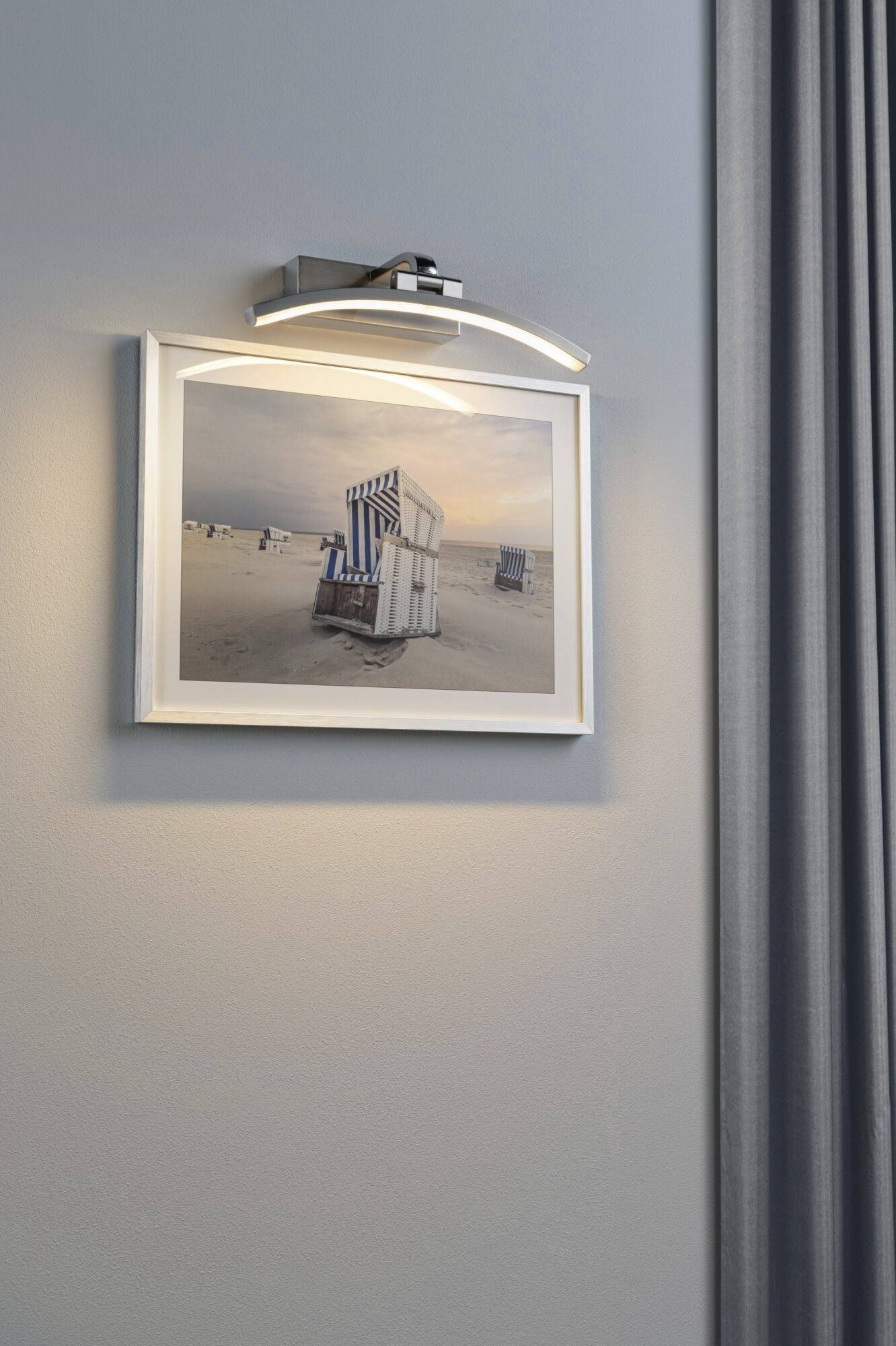 On the blue wall hangs an illuminated photograph of a beach chair on the beach at sunset. Beside it, a curtain can be seen.