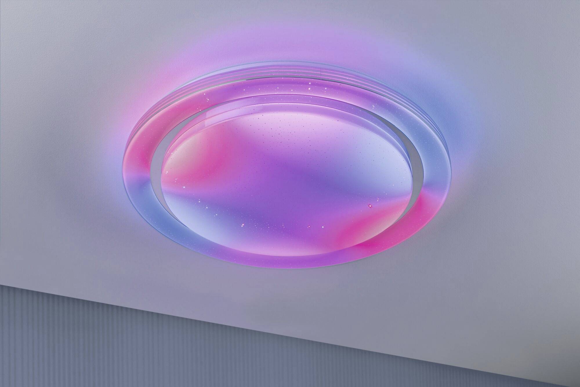 A ceiling-mounted, round light emits soft pink and blue light, creating a soothing atmosphere.