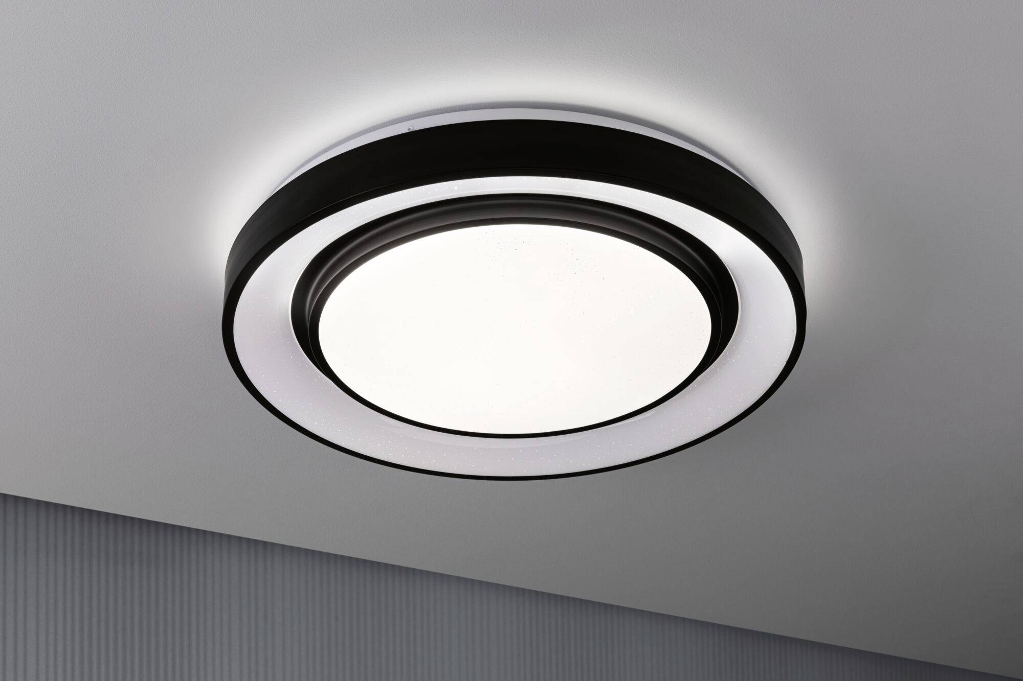 Round ceiling light with modern design, distributes even light. It is mounted on a white-painted ceiling.