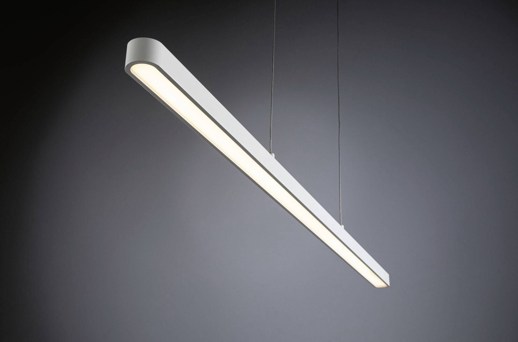 A modern, elongated ceiling light with a minimalist design hangs in a dark room, emitting soft, even light.