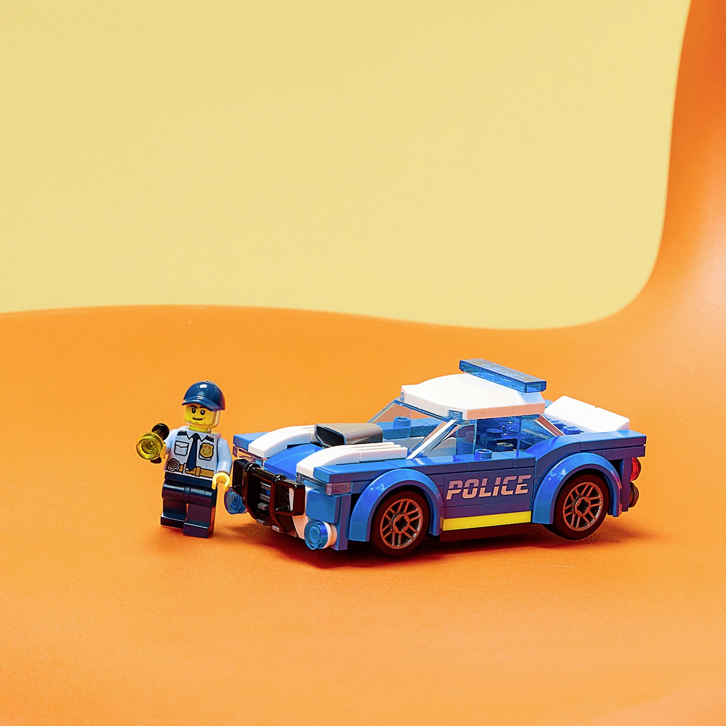 A Lego police officer stands beside a blue police car on an orange background.
