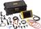A portable electric measuring device with cables and accessories is arranged next to a sturdy black case.