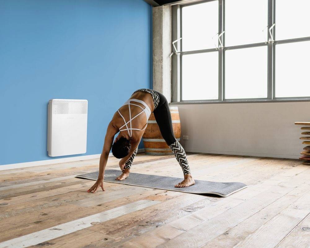 A person is doing yoga in a bright room with a wooden floor and blue walls. Light streams through large windows.
