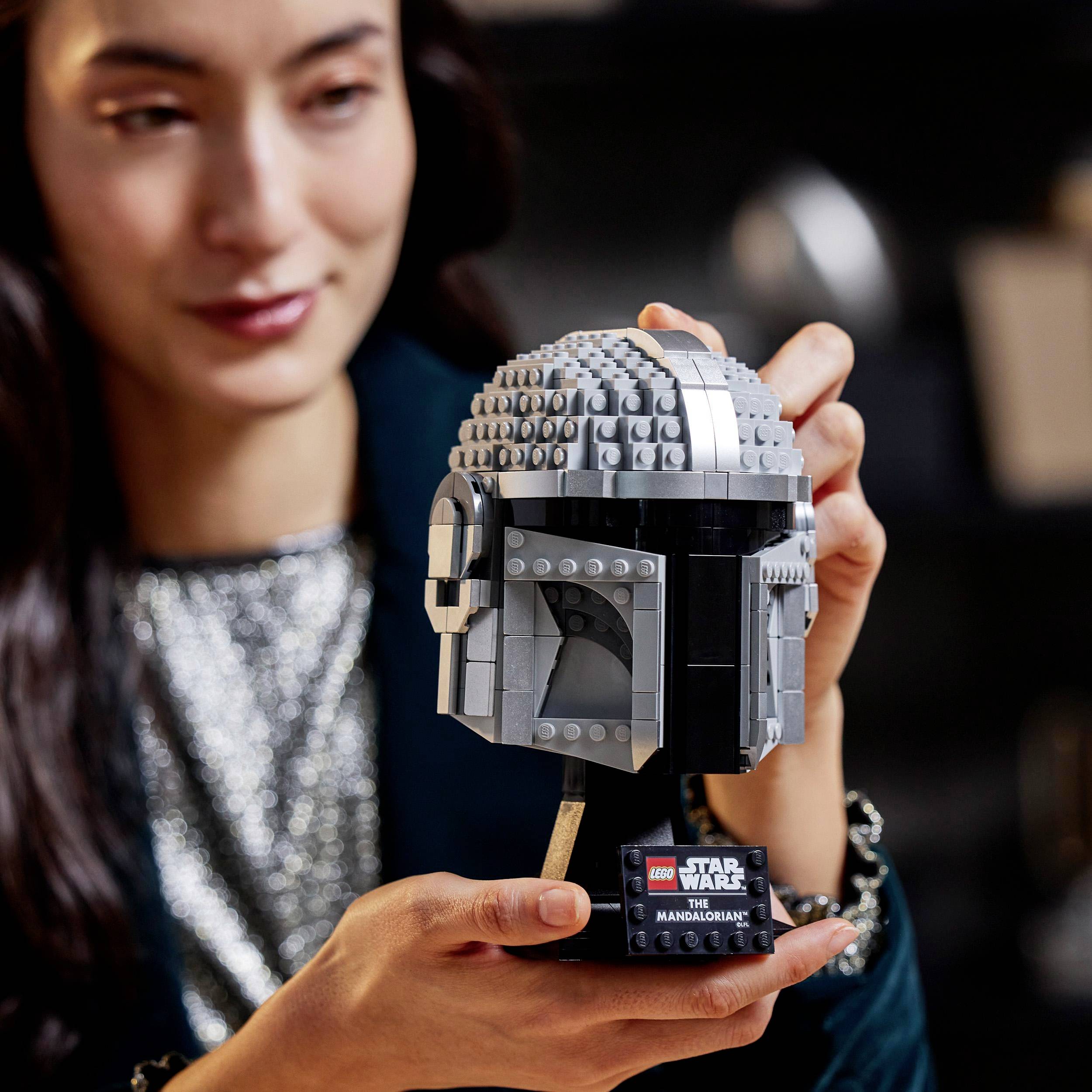 A person is holding a LEGO Star Wars helmet model in their hands, looking focused and intrigued, with a blurred background.
