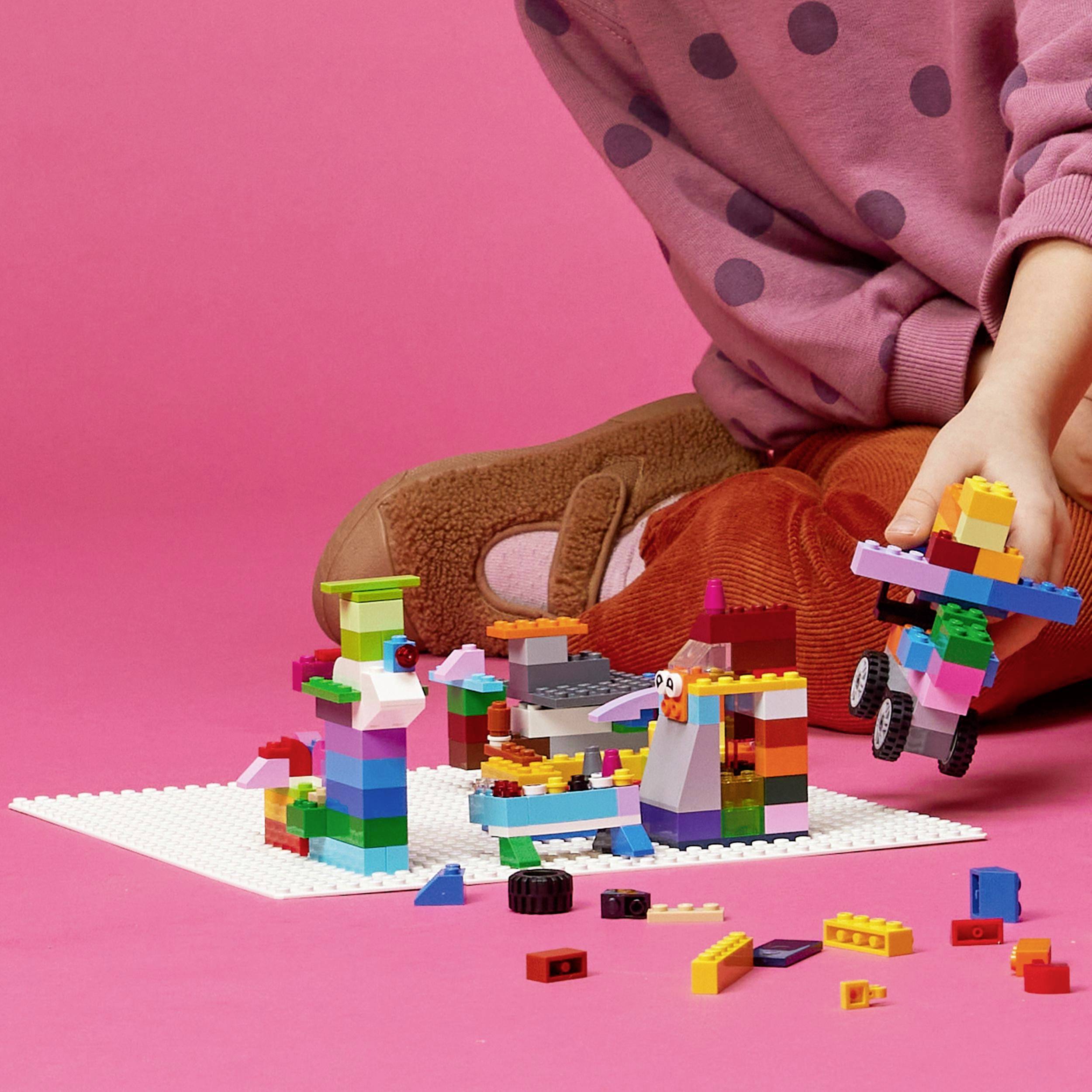 A child is playing with colourful Lego on the floor, wearing brown shoes and pink polka dot trousers.