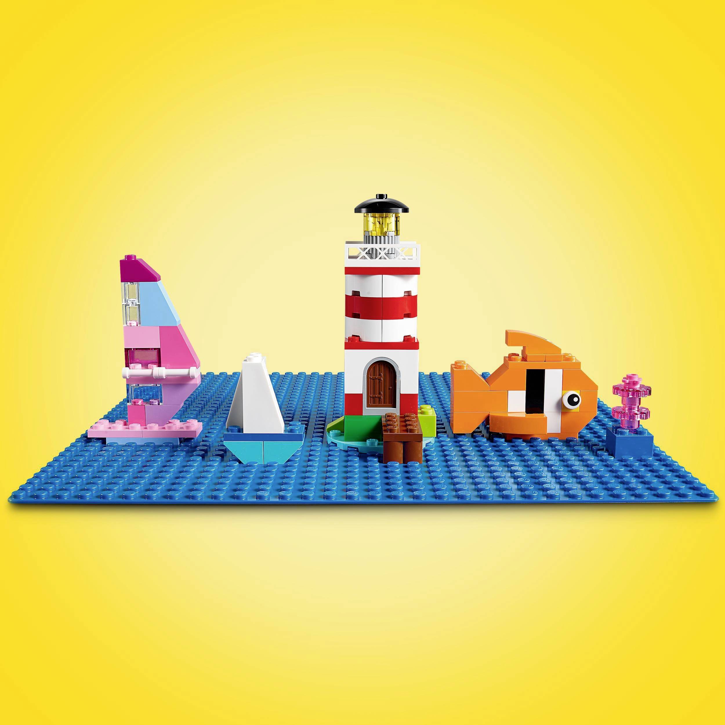 A set of building blocks shows from left to right: a pink and black sailing boat, a red and white lighthouse, and an orange and white fish, on a blue base plate.