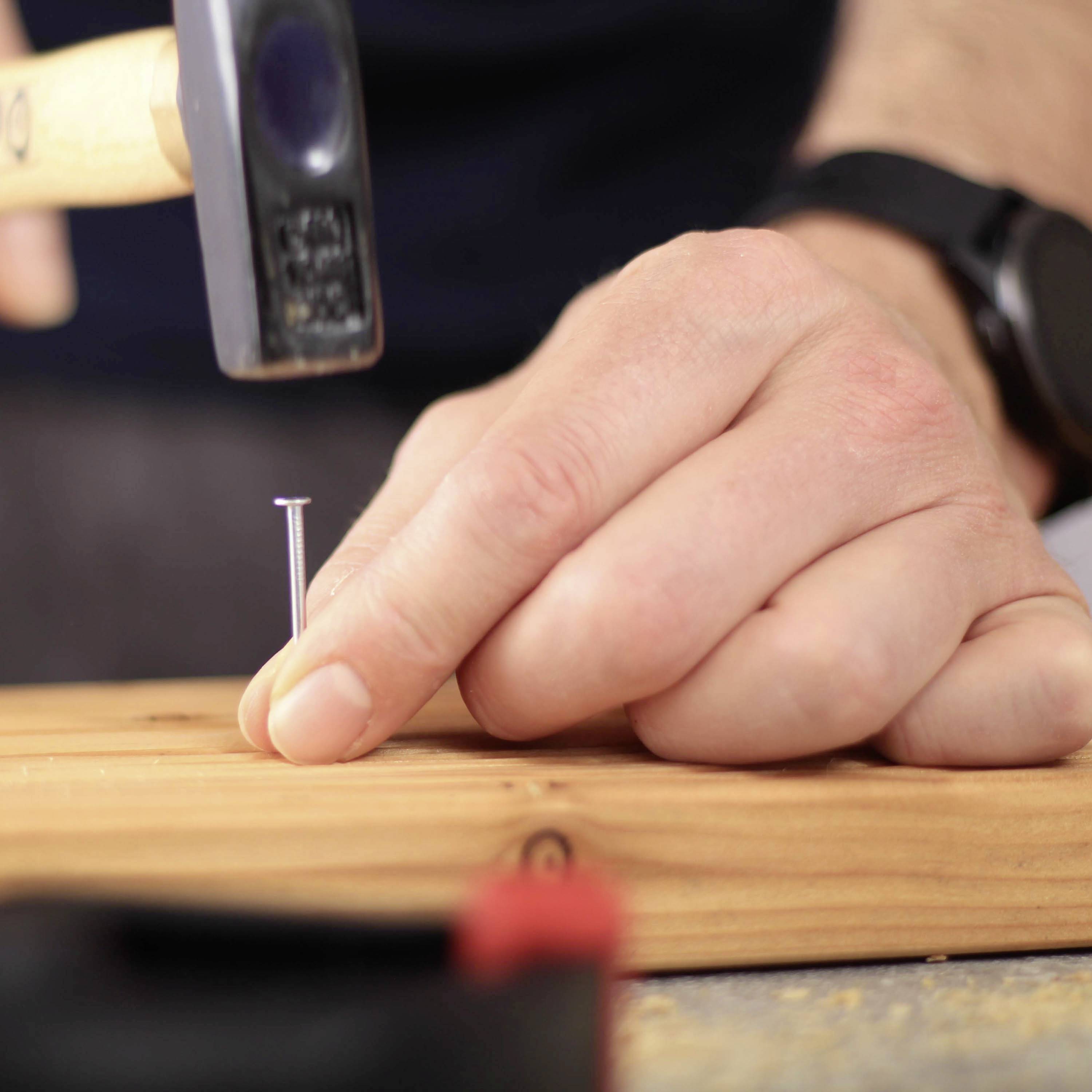 A hammer hovers over a nail held by a hand on a wooden board. DIY activities.