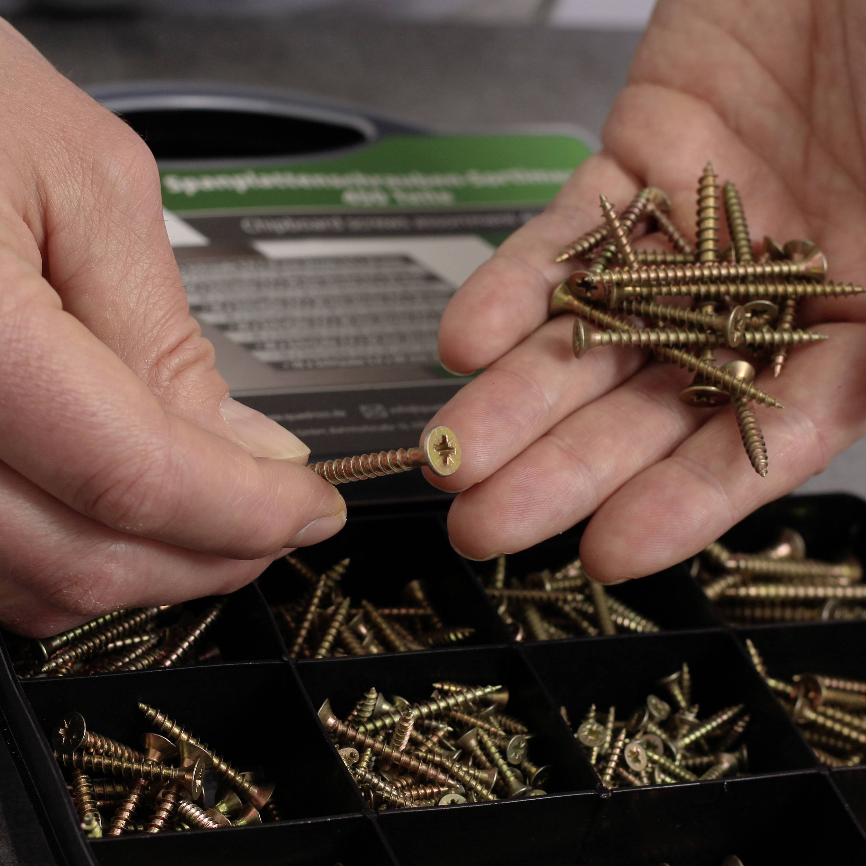 Two hands are holding wooden screws. One hand is pointing to a single screw, while the other holds several screws in its palm.