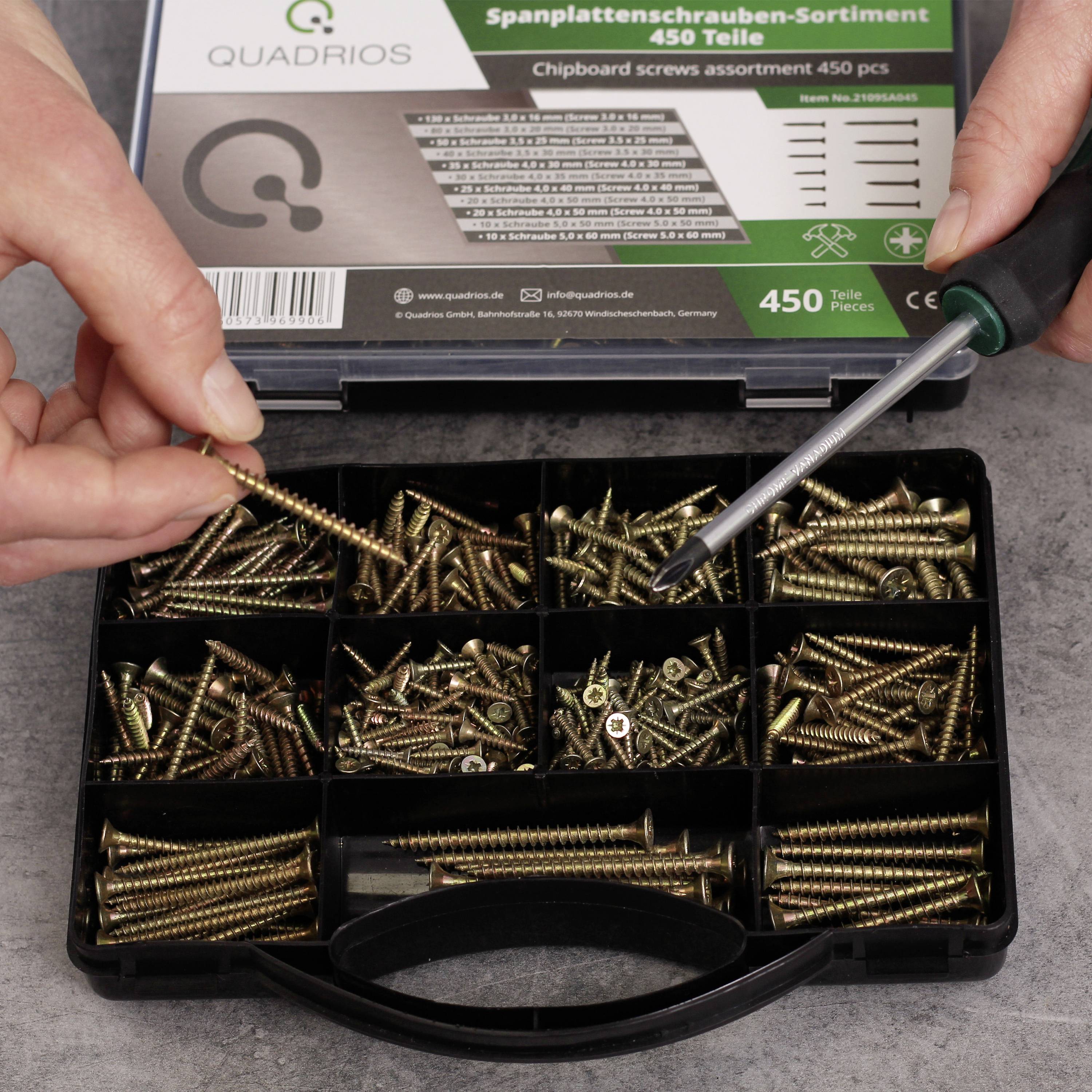 A person is holding a screwdriver over an open compartment box with various woodscrews.