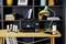 On a wooden table stands a printer with ink bottles beside it. In the background, a bookshelf and a green lamp are visible.