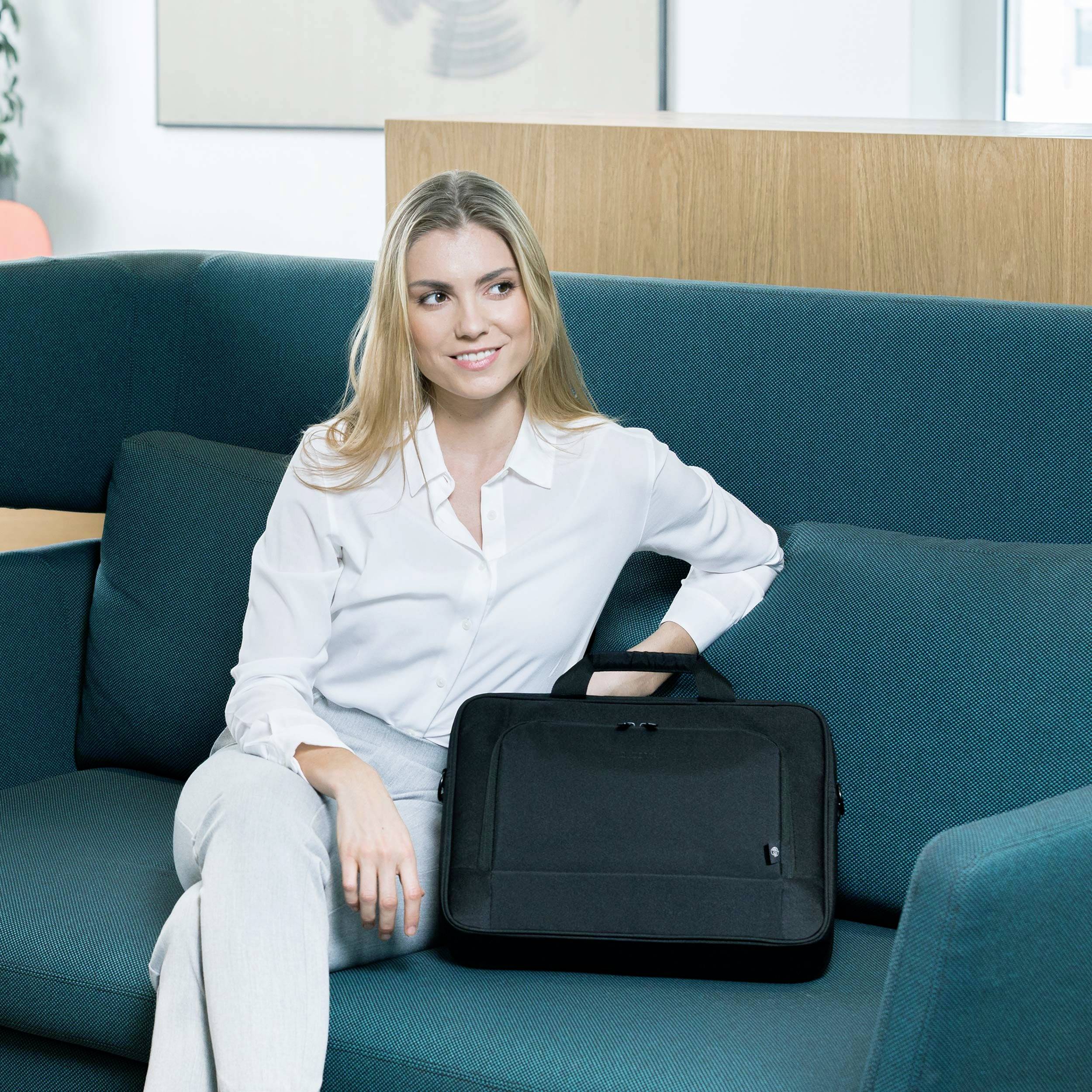 A woman in a white shirt is sitting on a green sofa and holding a black briefcase. Office furniture can be seen in the background.