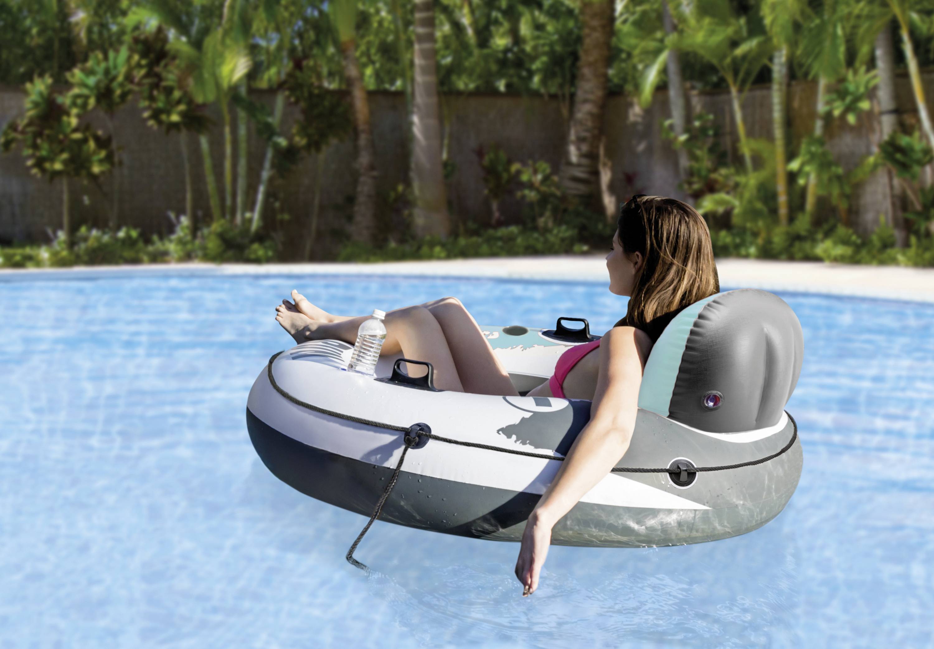 A woman relaxes in an inflatable chair on a pool. Surrounded by palm trees, she enjoys the sunny atmosphere.