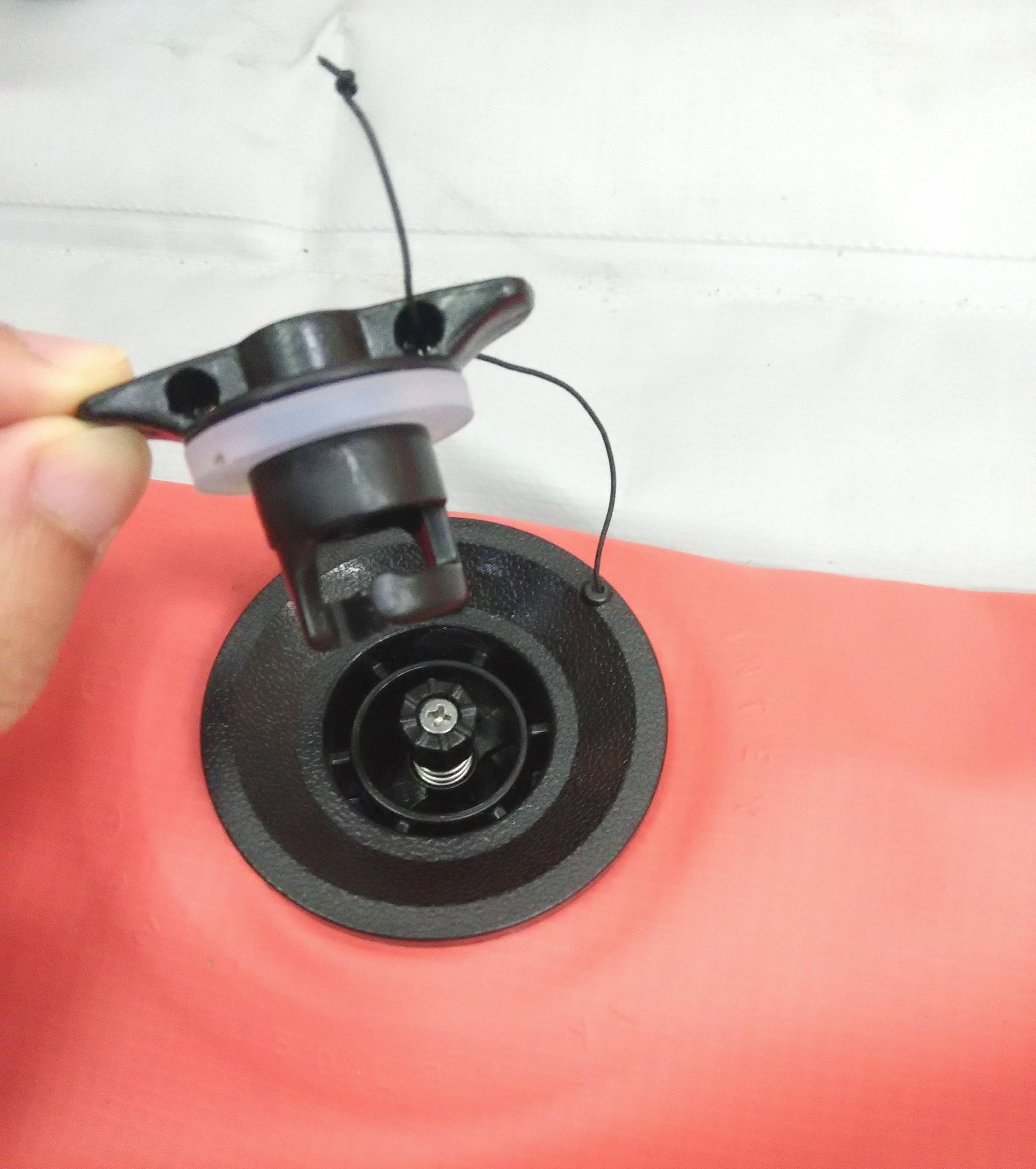Red inflatable boat base with one person holding an air valve by hand to open or close it.