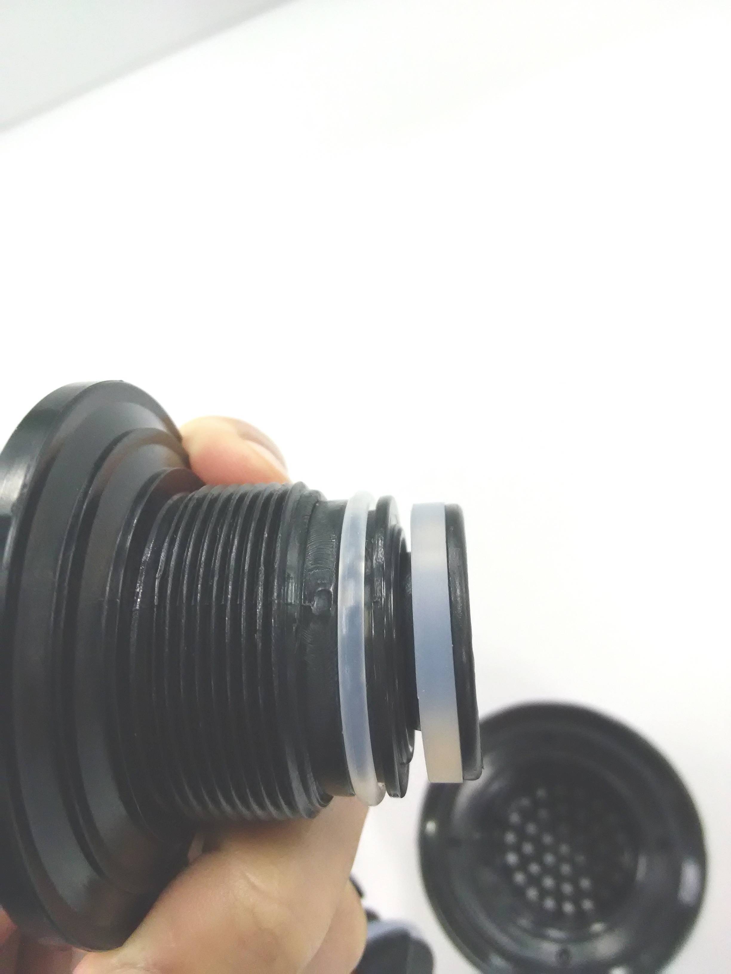 A hand is holding a black spare part with sealing rings. In the background, another part with a grille is visible.