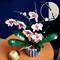 A Lego set of an orchid with white flowers and green stems on a round table.