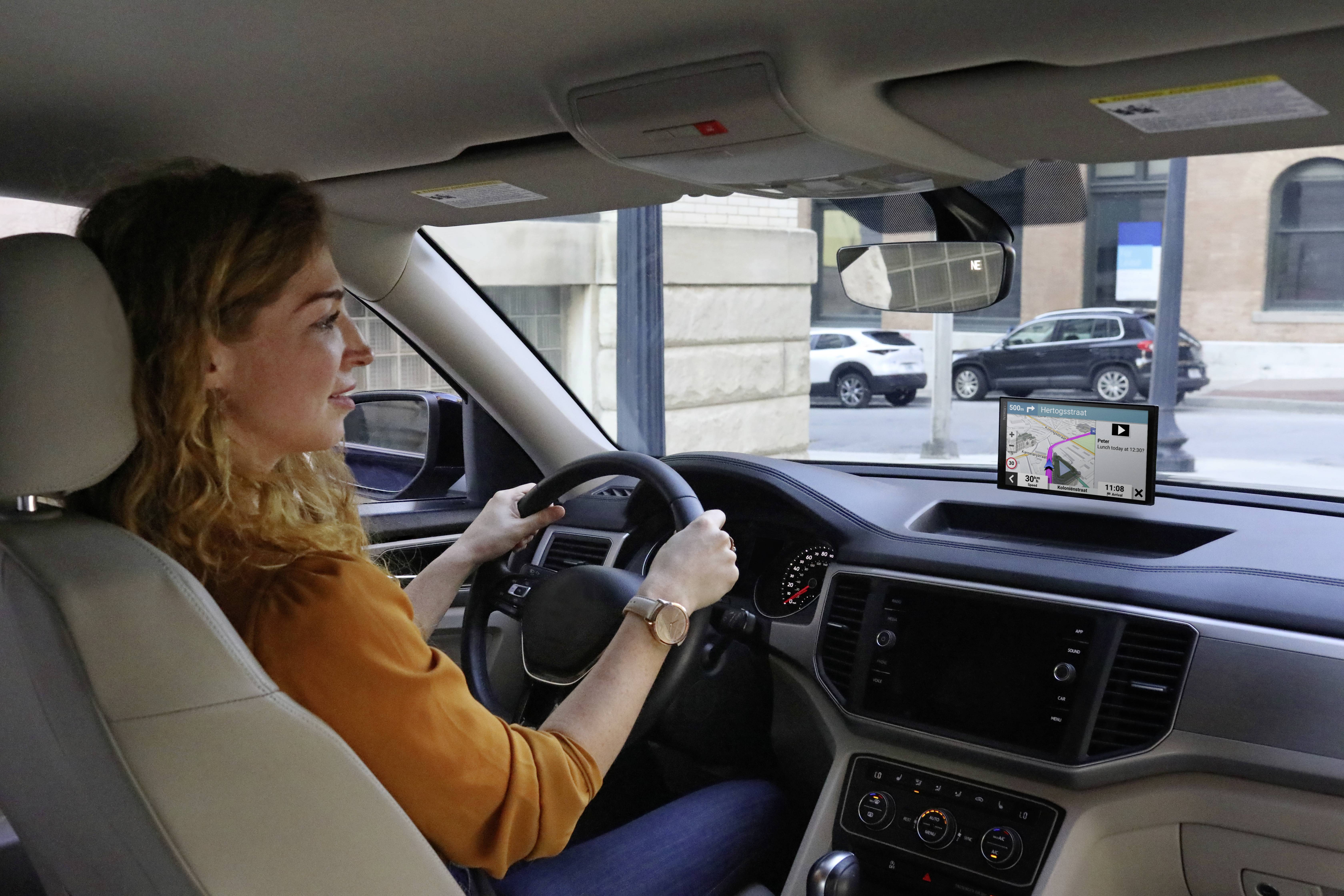 A woman is driving a car in the city. She glances at the sat-nav display, which shows a map with route information.