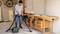 A person is vacuuming wood shavings in a workshop with an industrial vacuum cleaner next to a workbench.