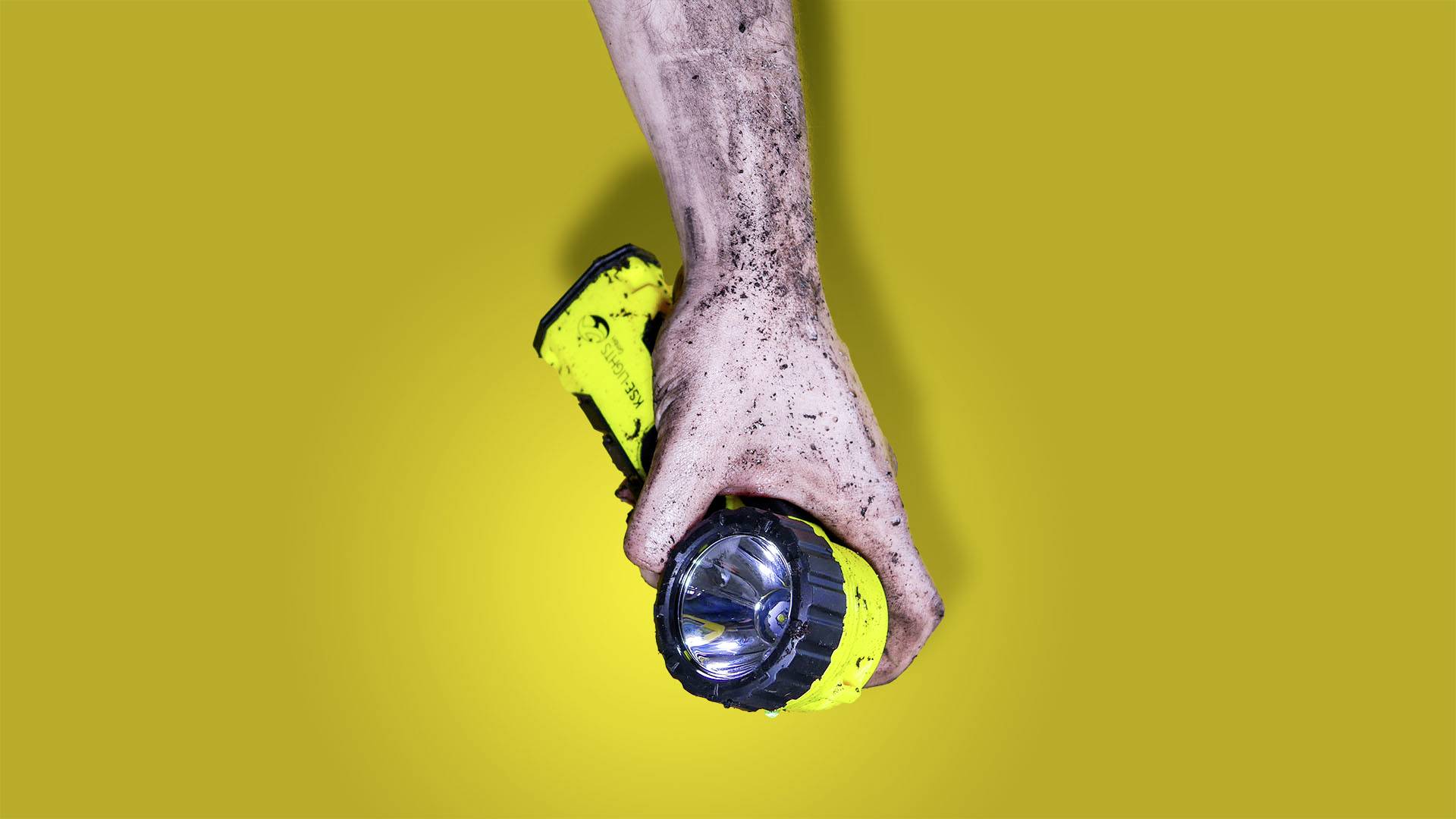 A muddy hand holds a yellow torch against a yellow background.<br><br>Note: I used "torch" instead of "flashlight" as this is the typical British English term for a handheld portable light source.