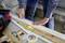 A person is measuring with a tape measure and applying protective tape to a wooden batten on a workbench in a workshop.