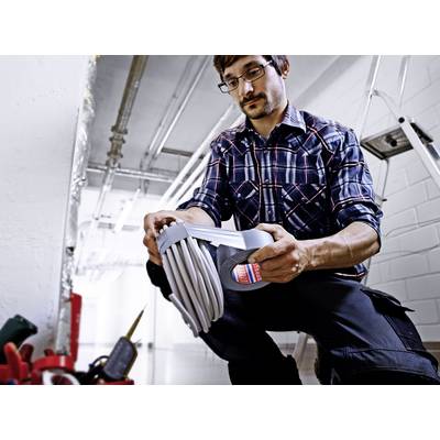 A person in work attire is kneeling before tools and checking a rolled-up hose packaging in an industrial space.