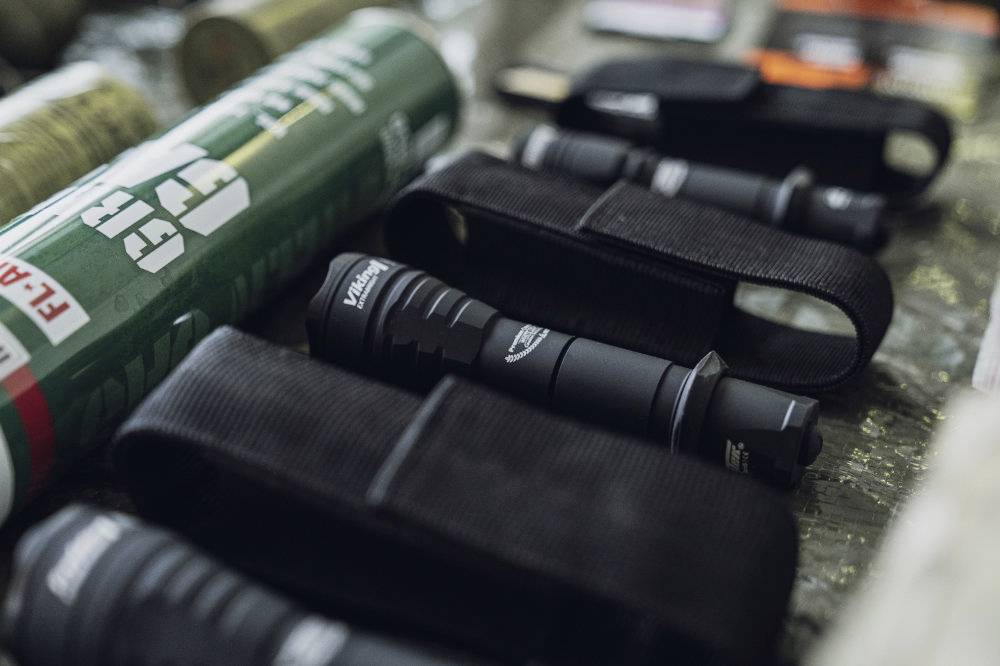 Close-up of several torches in black cases, lying on a table. A green cylinder blurred in the background.